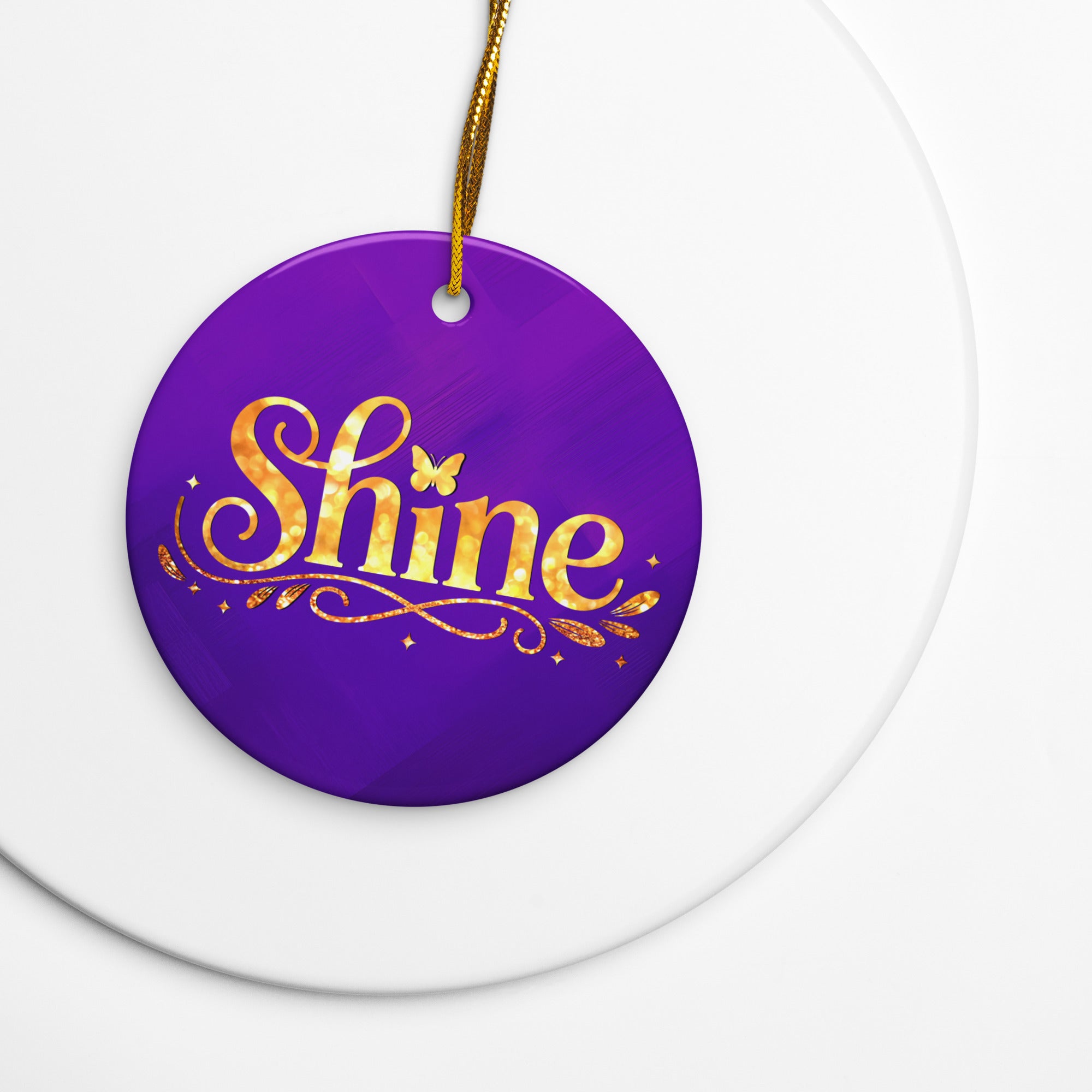 Glossy ceramic Christmas ornament with gold ‘Shine’ lettering on a midnight violet background, full gold string. Created by Women’s Fiction & Romance Author Juliet Gauvin.