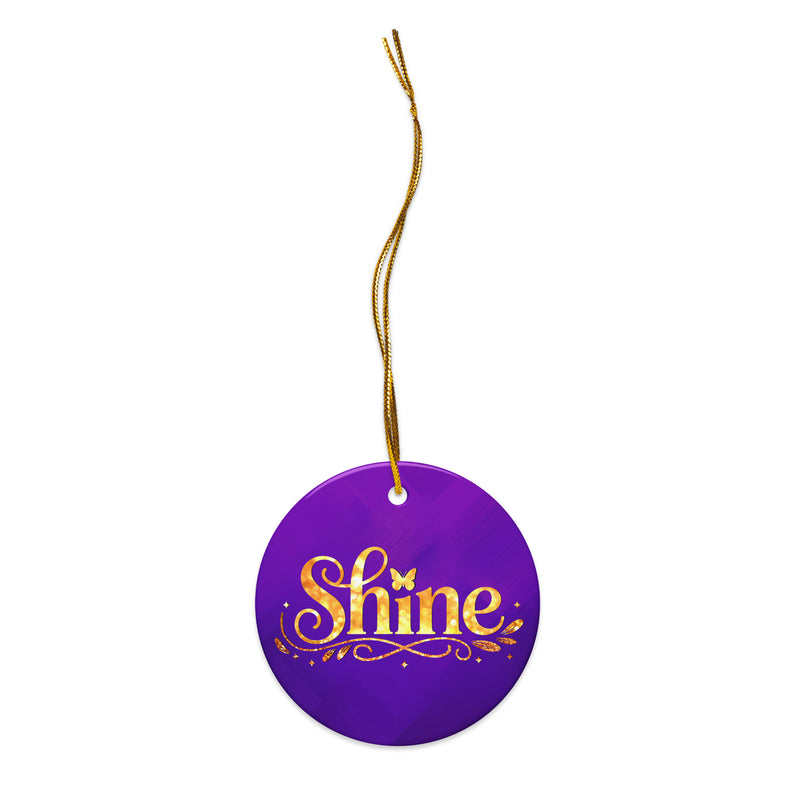 Glossy ceramic Christmas ornament with gold ‘Shine’ lettering on a midnight violet background, sitting on a white table. Created by Women’s Fiction & Romance Author Juliet Gauvin.