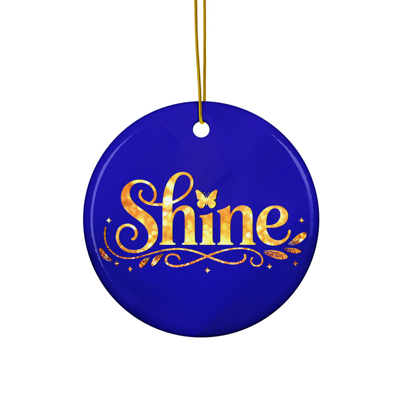 Glossy ceramic Christmas ornament with gold ‘Shine’ lettering on a midnight sapphire background, hanging from a gold string. Created by Women’s Fiction & Romance Author Juliet Gauvin.