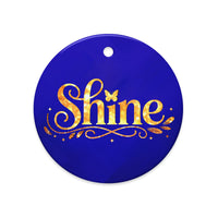 Glossy ceramic Christmas ornament with gold ‘Shine’ lettering on a midnight sapphire background. Created by Women’s Fiction & Romance Author Juliet Gauvin.