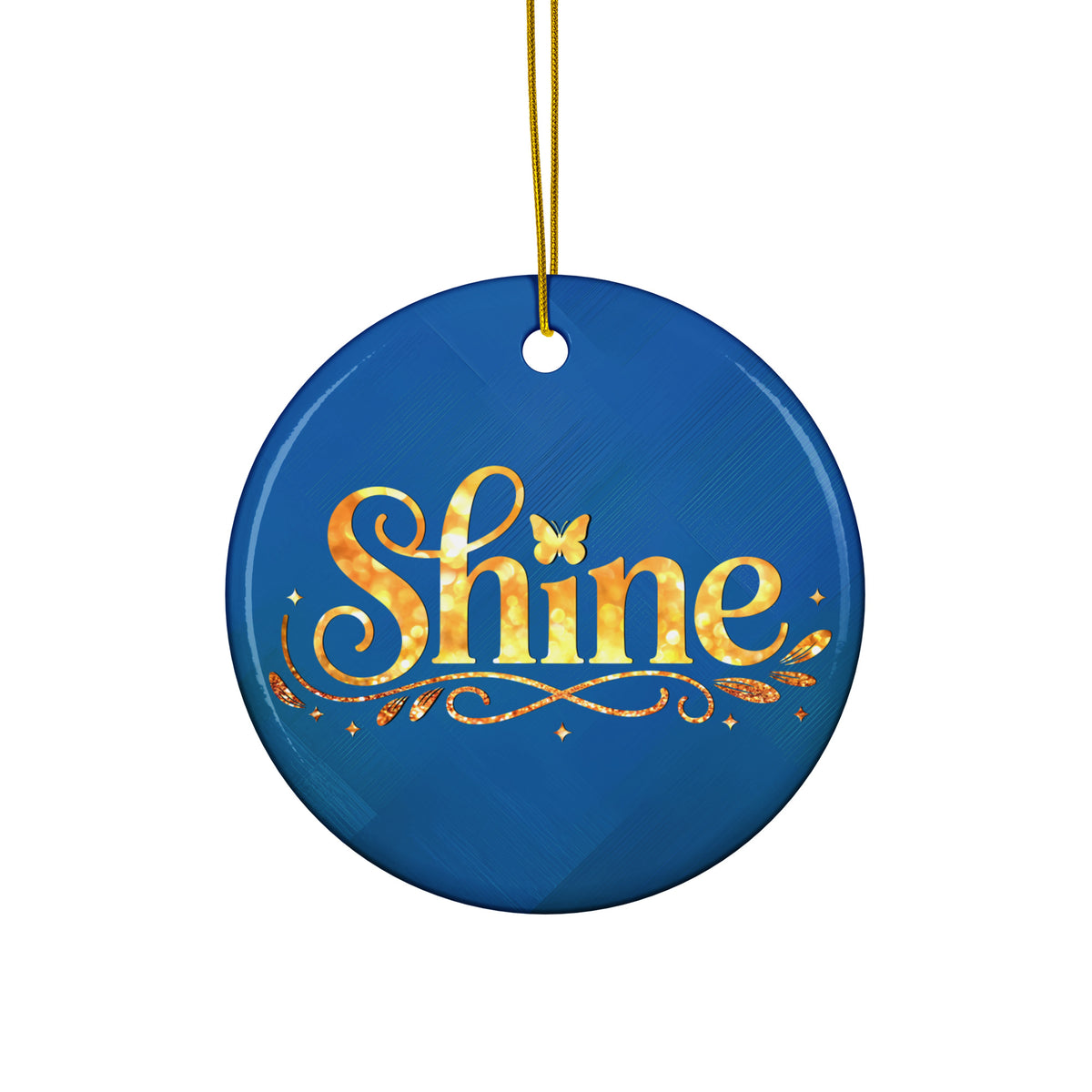 Glossy ceramic Christmas ornament with gold ‘Shine’ lettering on a midnight teal background, hanging from a gold string. Created by Women’s Fiction & Romance Author Juliet Gauvin.