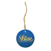Glossy ceramic Christmas ornament with gold ‘Shine’ lettering on a midnight teal background, full gold string. Created by Women’s Fiction & Romance Author Juliet Gauvin.