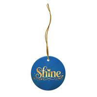 Glossy ceramic Christmas ornament with gold ‘Shine’ lettering on a midnight teal background, full gold string. Created by Women’s Fiction & Romance Author Juliet Gauvin.