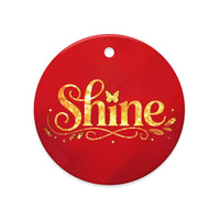 Glossy ceramic Christmas ornament with gold ‘Shine’ lettering on a mags red background. Created by Women’s Fiction & Romance Author Juliet Gauvin.